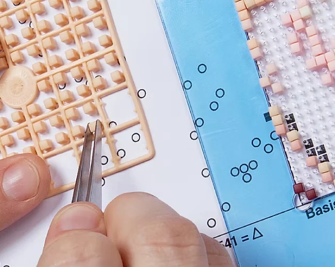 Hands picking a pixel from a pixelsquare with tweezers, above the pattern and baseplate